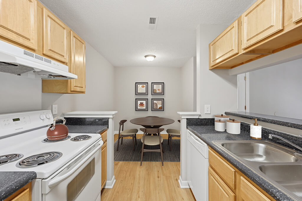 A kitchen with white appliances and wooden cabinets at the Greens of Pine Glen Apartments in Durham, North Carolina.